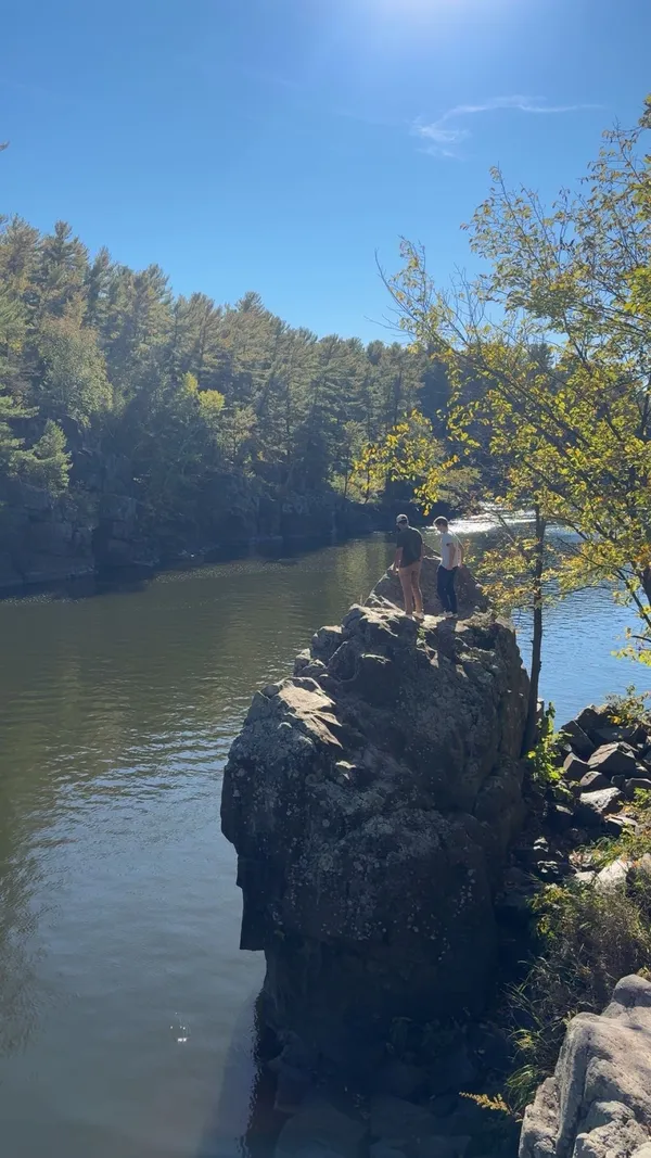 A rocky bluff over a river on a sunny day, with trees along the far shore.